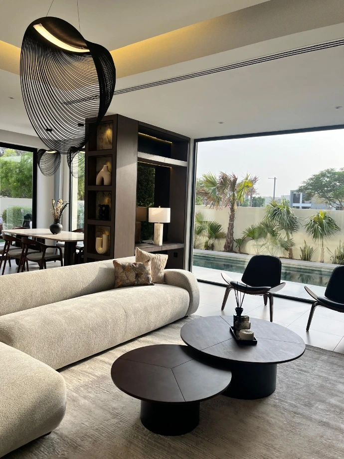 Architecture d'intérieur Nice Hunter Design à Dubai Hills : Salon de luxe avec canapé courbe en bouclé, suspension design monumentale et baie vitrée ouvrant sur une piscine privée.