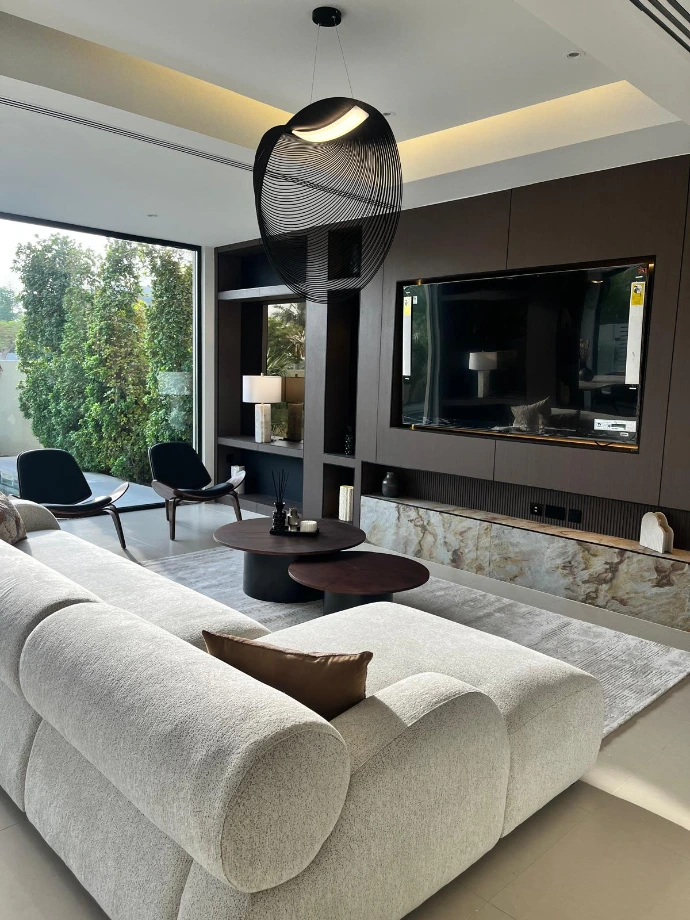 Conception de mobilier sur mesure par Nice Hunter Design : Meuble TV mural en noyer avec niches rétroéclairées et soubassement en marbre veiné dans une villa de prestige à Dubaï.