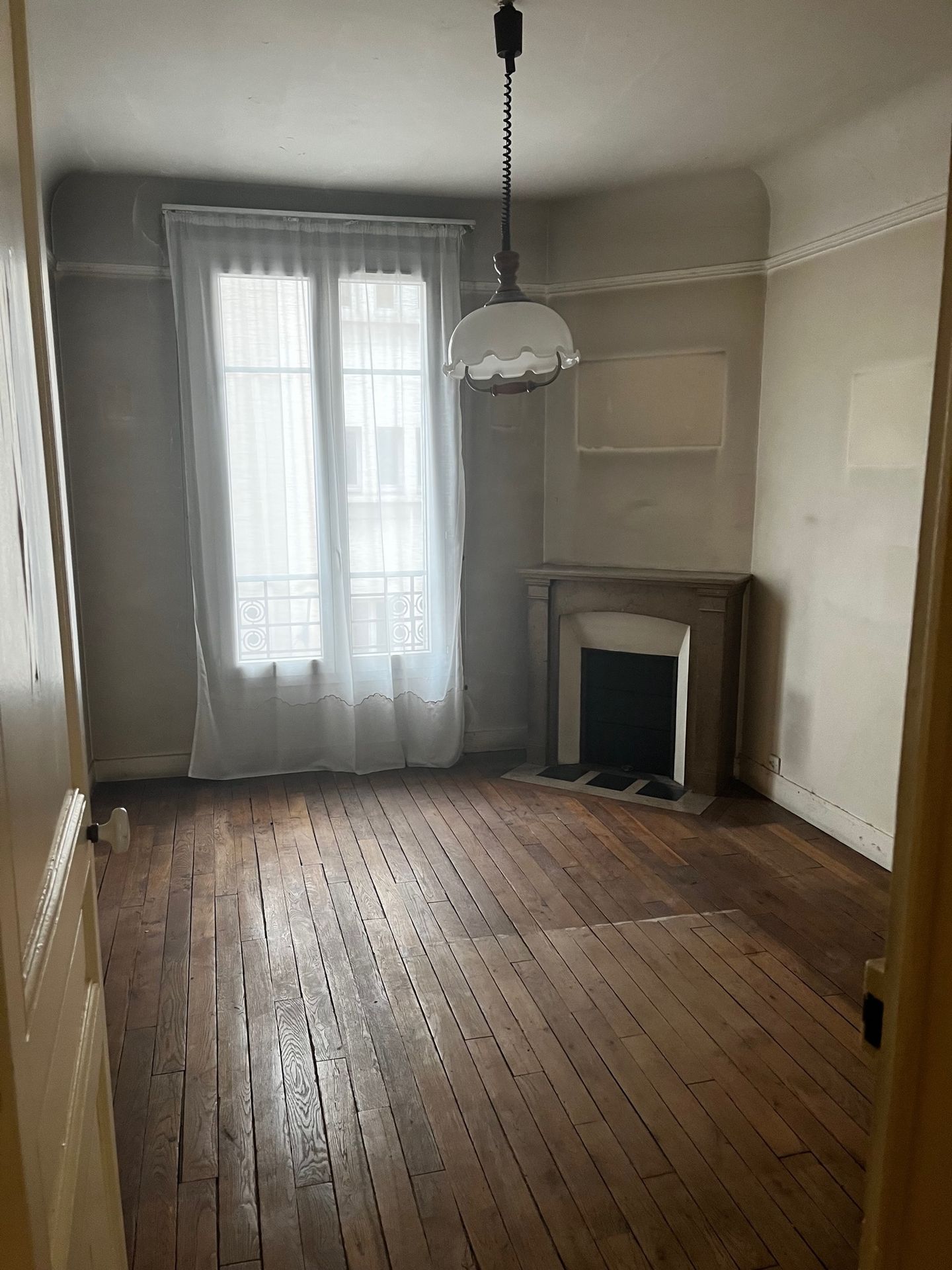 Pièce de vie lumineuse vide avec moulures et parquet ancien en cours de projet.